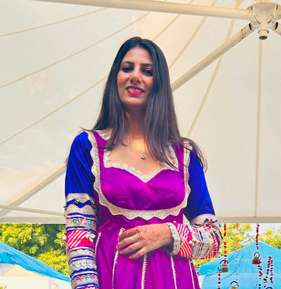 Woman in a purple and blue traditional outfit standing under a large white umbrella.
